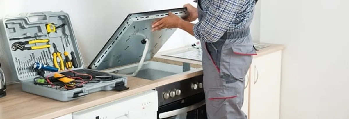Cooktop repair technician lifting a built-in stovetop for service in Fort Lauderdale, FL